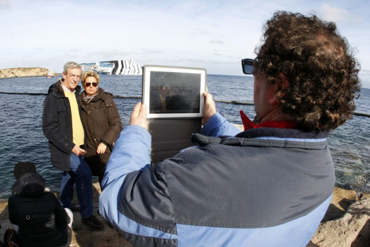 People take a picture on a rock in front of the Costa Concordia cruise ship which ran aground off the west coast of Italy