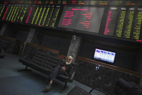 Trader sits on couch underneath an electronic board displaying share prices at Karachi Stock Exchange