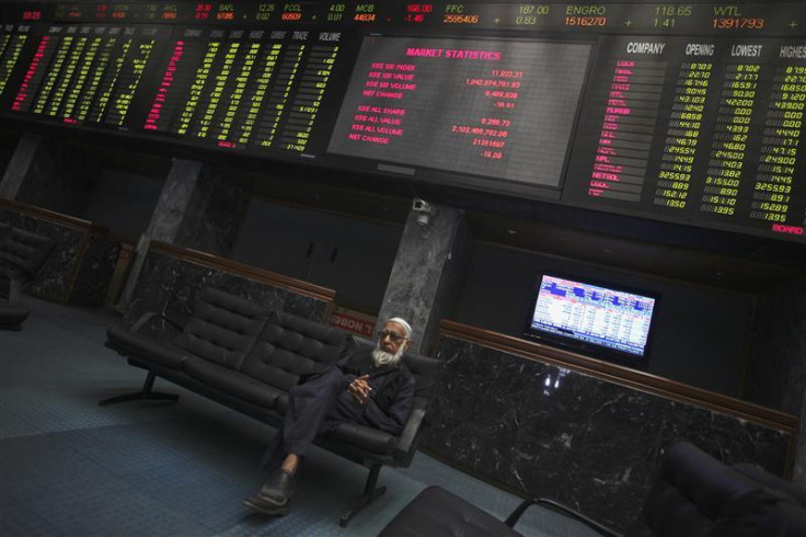 Trader sits on couch underneath an electronic board displaying share prices at Karachi Stock Exchange