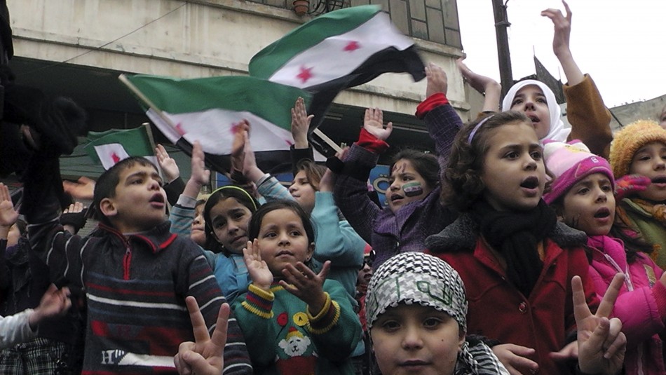 Children chant slogans as Syrian independence flags are waved behind them during a protest against Syrias President Bashar al-Assad in Khalidieh, near Homs