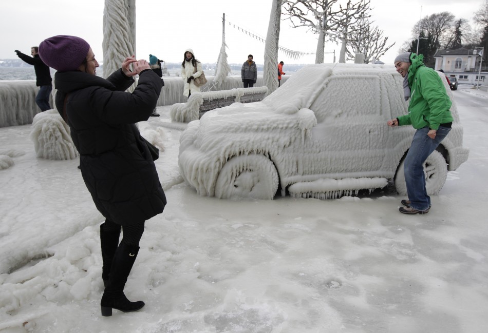 A woman takes a picture of a man near an ice covered car in Versoix near Geneva