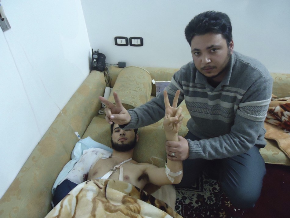 A man flashes a victory sign and holds up the arm of a man wounded on February 5, 2012, also flashing a victory sign, in Baba Amro, a neighbourhood of Homs