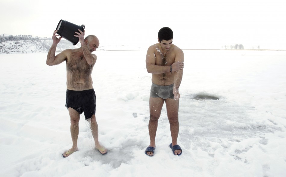 A man pours water on himself as another rubs himself with snow on the ice-covered Lisi Lake