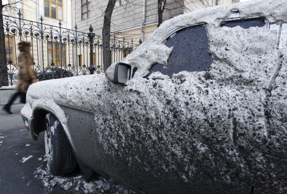 A woman passes by a car, covered with snow and dirt, during winter in central Moscow