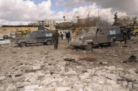 Syrian security personnel inspect damaged riot police vehicles