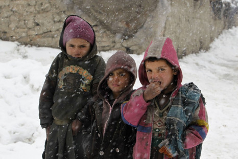 Afghan children pose for a photo as they stand in the snow outside their shelter at a refugee camp in Kabul
