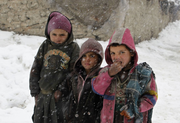 Afghan children pose for a photo as they stand in the snow outside their shelter at a refugee camp in Kabul