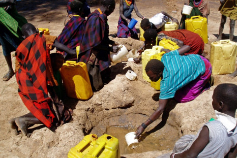 gandan women and children collect water from a hole dug in a dry riverbed at Kaabong village, Karamoja region