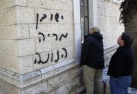 Church workers stand next to a church wall sprayed with graffiti in Jerusalem
