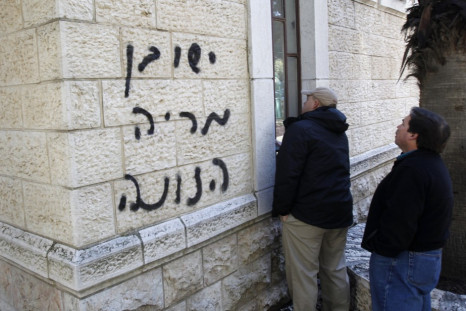 Church workers stand next to a church wall sprayed with graffiti in Jerusalem