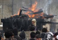 Afghan men stand near a pile of wood and tyres, set on fire by the protesters, during a protest outside the U.S. military base in Bagram