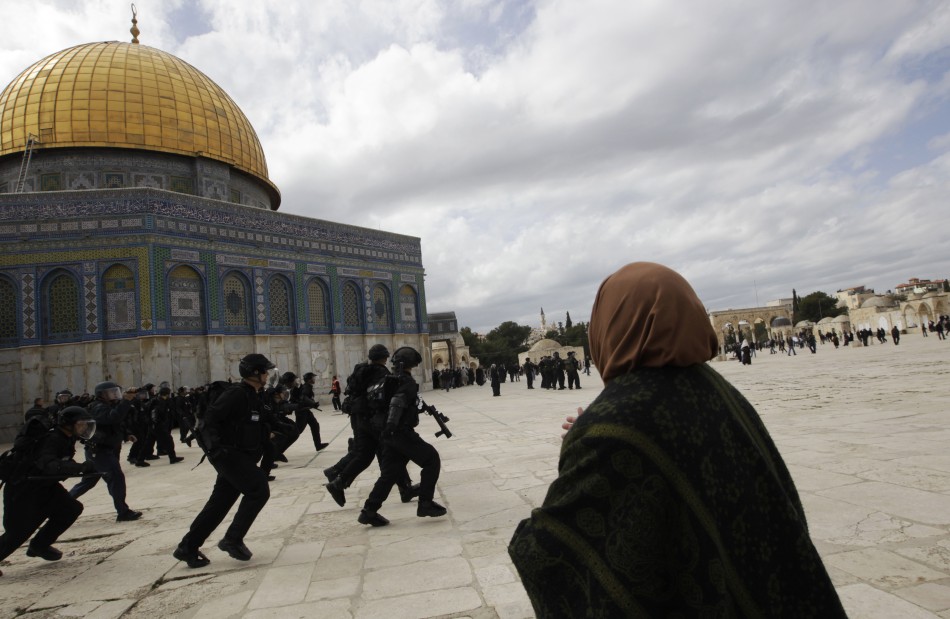 A Palestinian woman gestures at Israeli policemen as they run with their weapons during clashes with Palestinian protesters at the Temple MountNoble Sanctuary