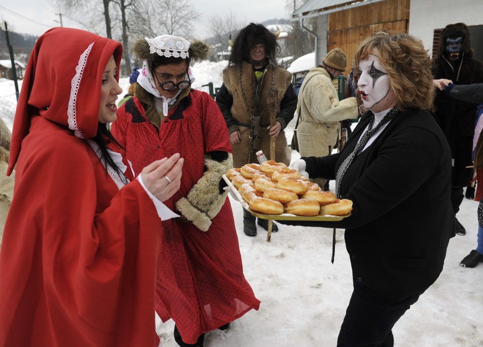 A villager dressed in a mime costume serves donuts to others during a carnival in the village of Lazy pod Makytou