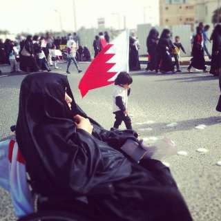 A child waving Bahrains flag walks as the demonstartion reach an end, while a women is sitting down.