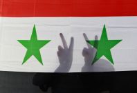A Syrian protester gestures victory signs behind their national flag