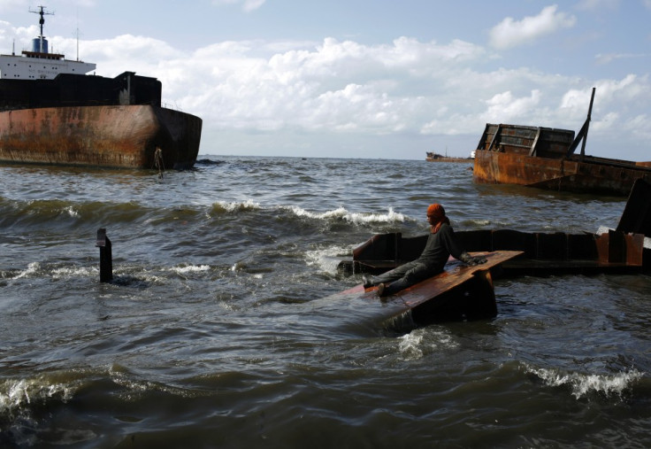 A worker rests on a metal scrap near old ships that are to be recycled at a demolition site in Jakarta