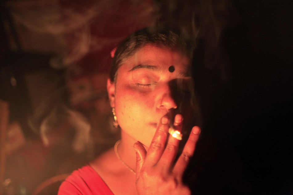 Seventeen-year-old Hashi smokes a cigarette inside her room before she serves a customer at Kandapara brothel in Tangail, a northeastern city of Bangladesh