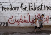 Palestinian girls walk past wall scrawled with graffiti in Dehaishe refugee camp, Bethlehem