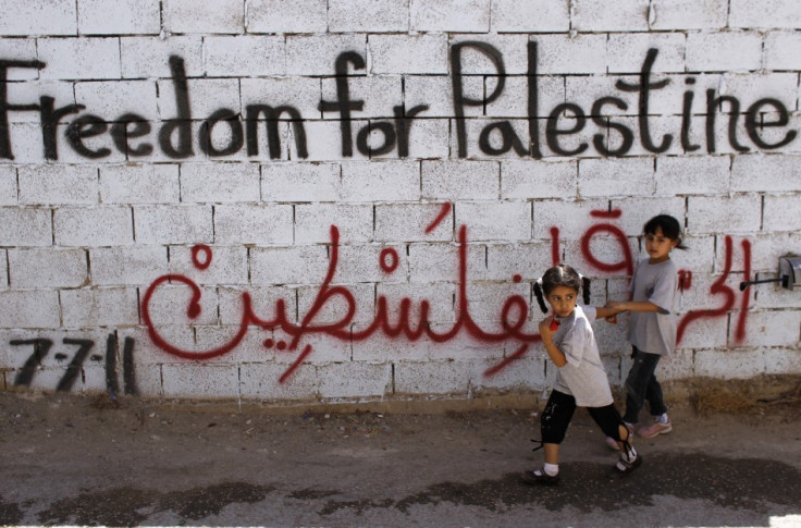 Palestinian girls walk past wall scrawled with graffiti in Dehaishe refugee camp, Bethlehem