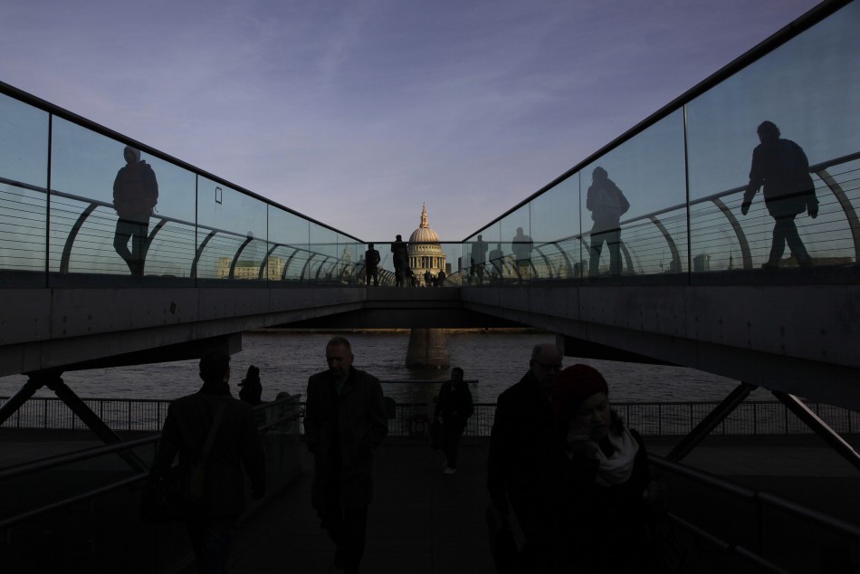 St Pauls Cathedral is seen during sunrise as pedestrians walk across the Millennium Bridge in the City of London