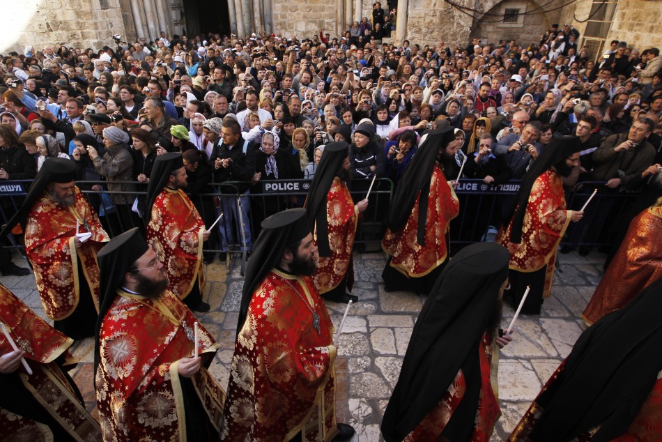 Members of the Greek Orthodox clergy hold candles as they walk past the crowd