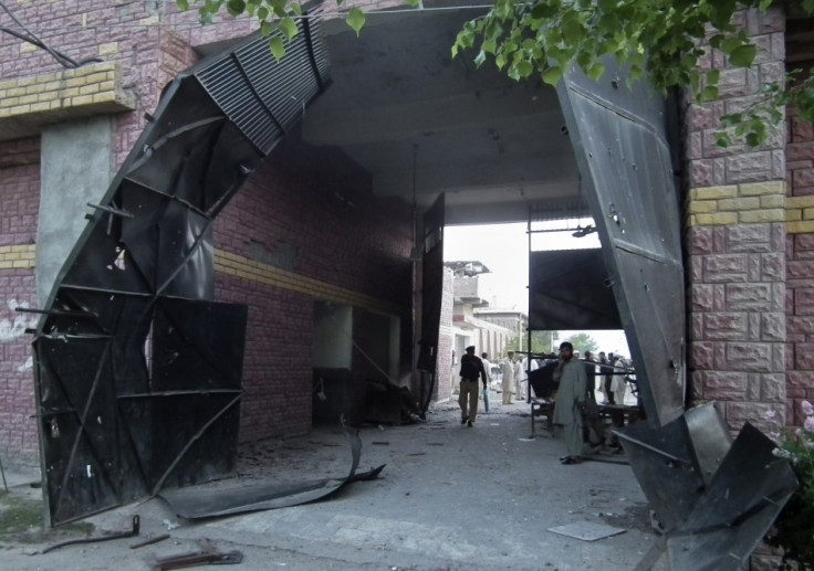 Policeman and security official stand near a damaged jail gate after inmates escaped from the prison in the town of Bannu