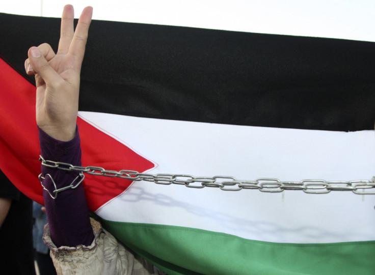 A  woman flashes the peace sign in front of the Palestinian flag