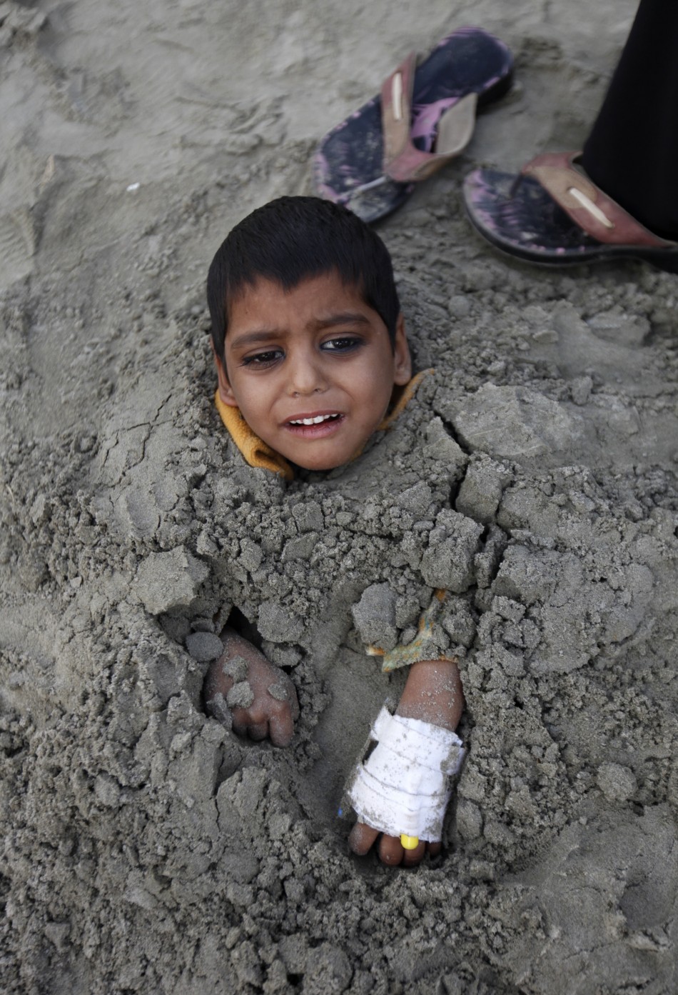 Yasir, a seven-year-old handicapped boy, lies buried in sand up to his neck during a partial solar eclipse at Karachis Clifton beach