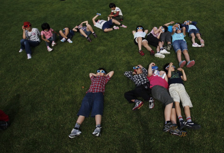 School children using solar viewers lie down on a lawn as they observe an annular eclipse at Hirai Daini Elementary School in Tokyo
