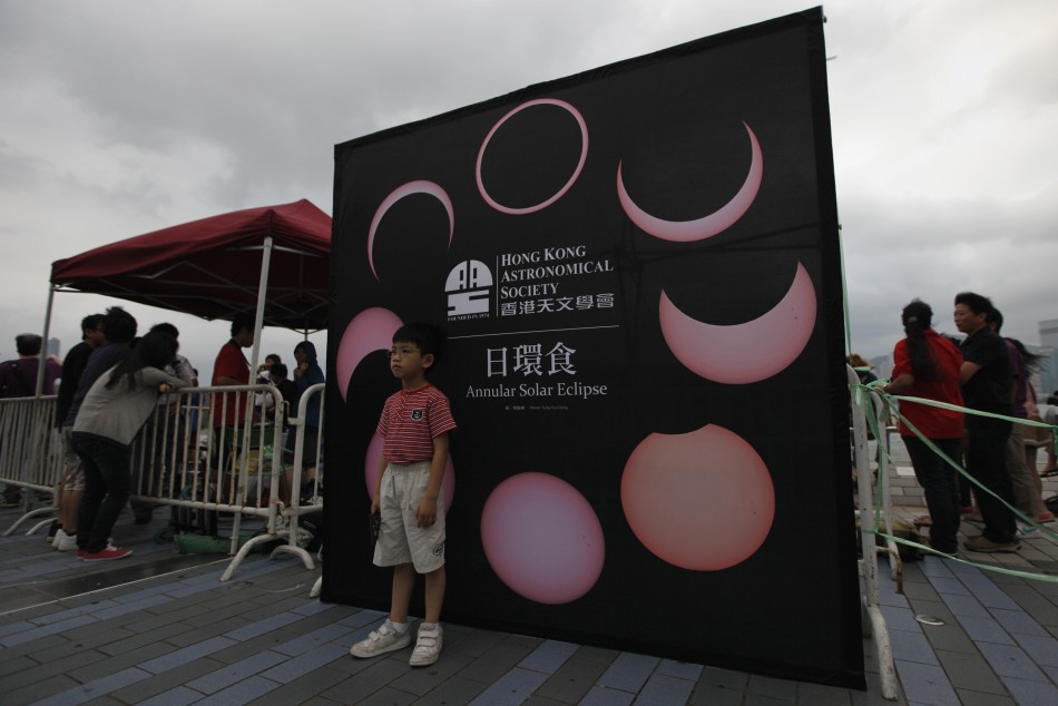 A child poses for pictures in front of a board, which shows the different phases of an annular solar eclipse, in Hong Kong