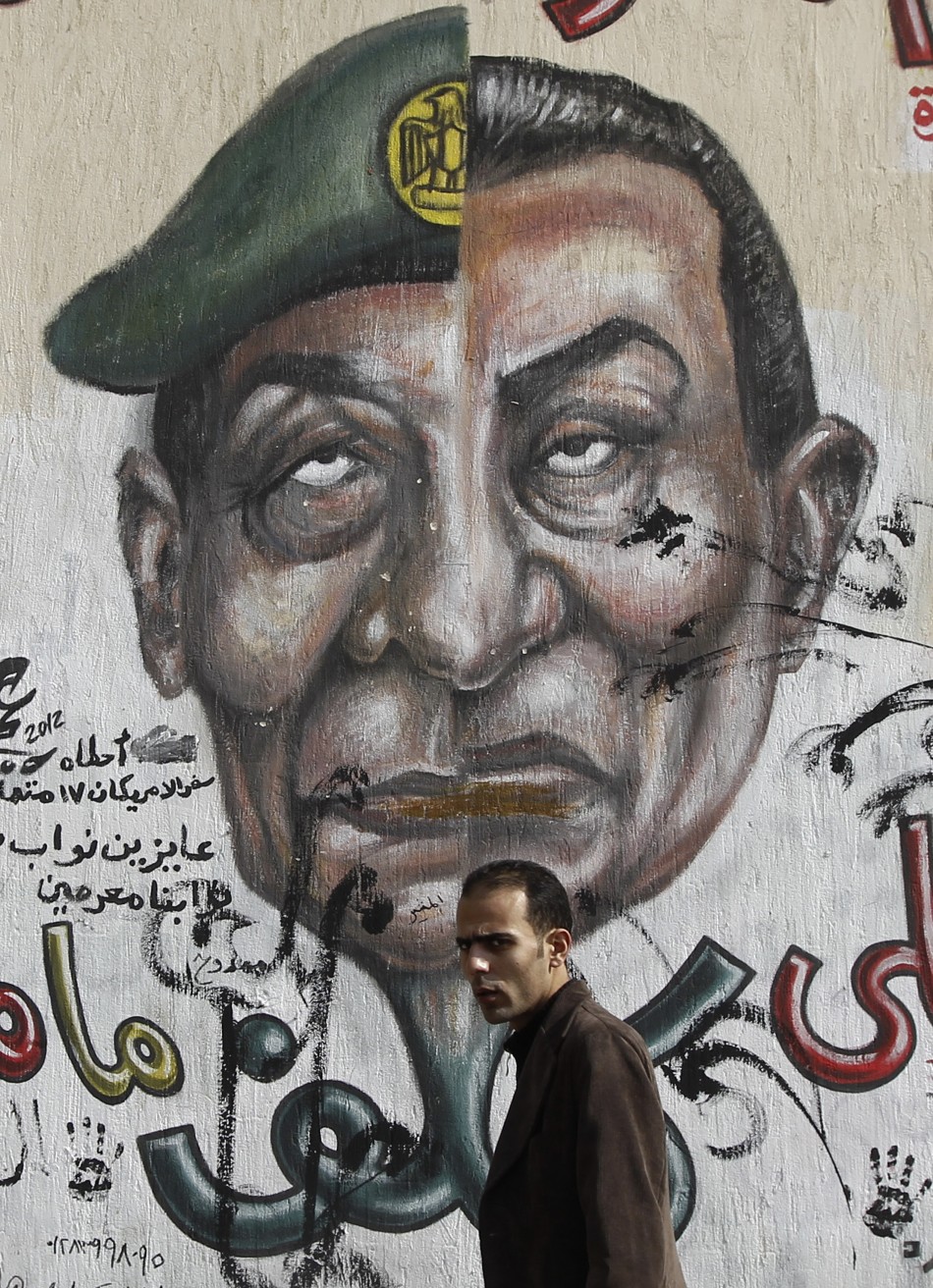 Egyptian man walks in front of a wall sprayed with graffiti depicting the faces of former President Mubarak and Field Marshal Tantawi in Cairo