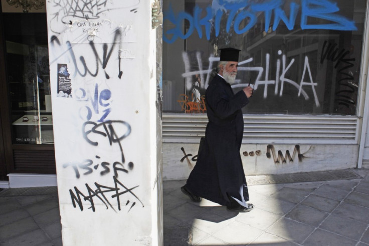 A Greek Orthodox priest walks past a closed shop in central Athens (Photo: REUTERS)