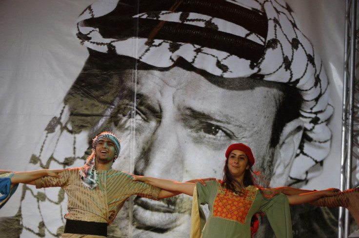 Palestinian dancers perform in front of a banner depicting late Palestinian leader Yasser Arafat