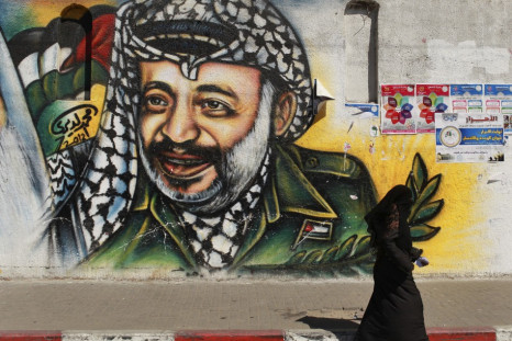 Palestinian woman walks past a mural depicting late leader Arafat in Gaza