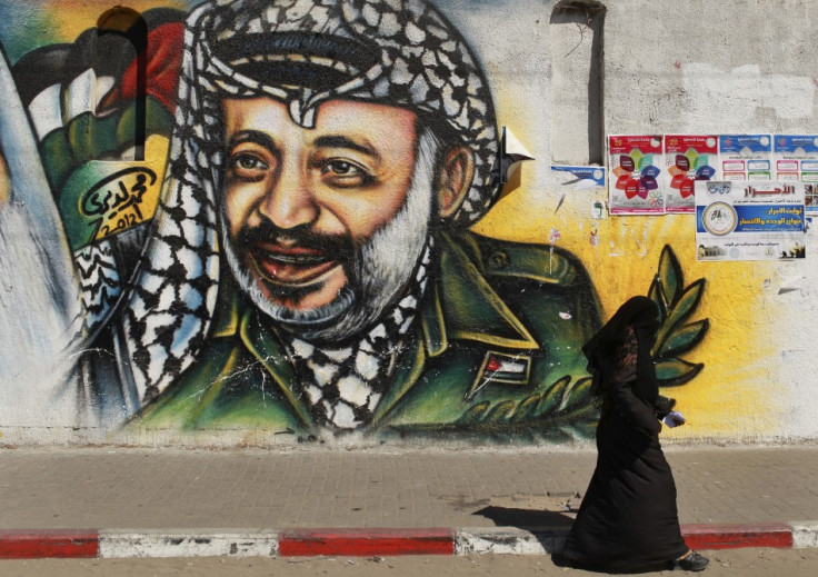 Palestinian woman walks past a mural depicting late leader Arafat in Gaza