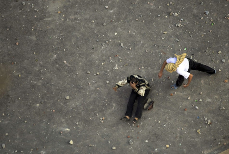 An anti-Muslim Brotherhood demonstrator prepares to throw stones as another falls on the ground injured during clashes