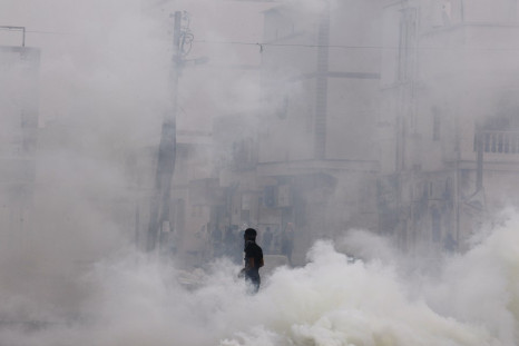 An anti-government protester walks through tear gas during clashes with riot police in the village of Mameer