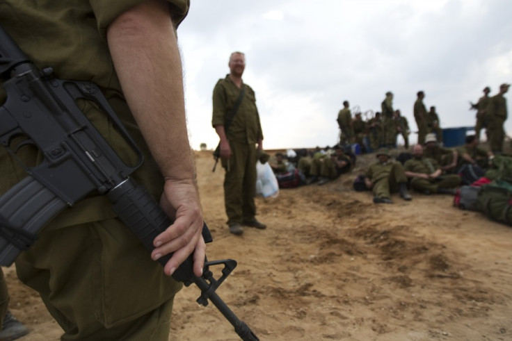 An Israeli reservist soldier holds his weapon as others wait with their gear before going home,