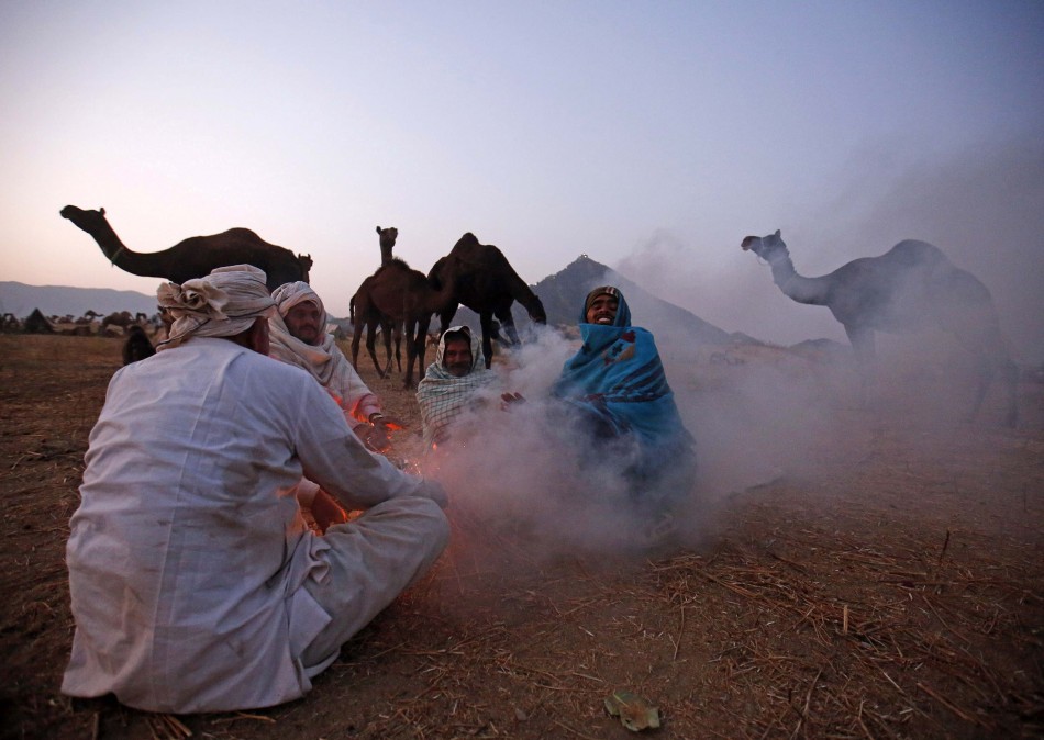 Camel herders sit around a bonfire to warm themselves as they wait for customers at Pushkar Fair in Rajasthan