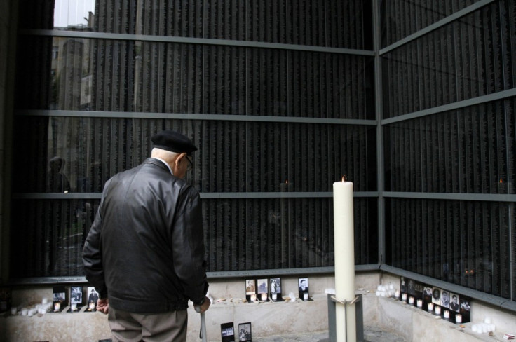 A man stands in front of a wall bearing the names of victims during the Holocaust memorial day