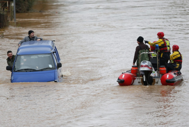 Firemen in a rescue dingy pass a van driving along a flooded street on the outskirts of Gloucester (Reuters)