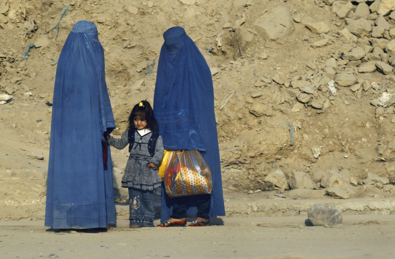 Afghan women clad in burkas wait for transportation on a road in Kabul