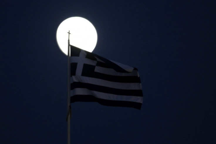 A Greek flag flutters in front of the moon in Athens