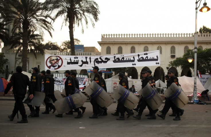 Riot police walk past a banner with a defaced photo of the Muslim Brotherhood's supreme guide, Mohamed Badie, in Cairo