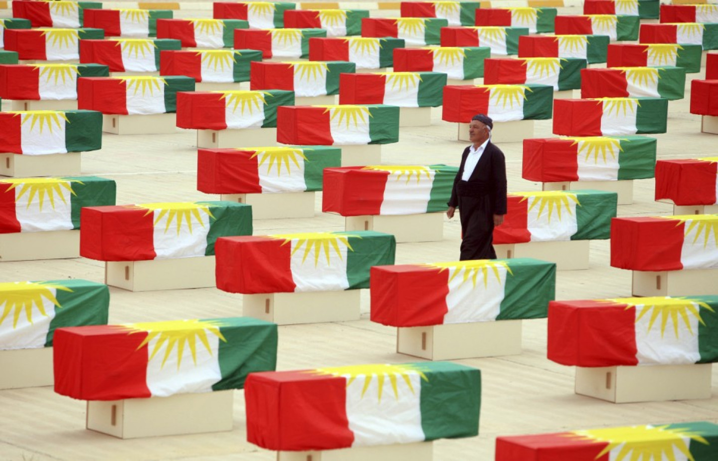 A Kurdish man walks between coffins draped with Kurdish flag containing the remains of victims during a burial ceremony in Sulaimaniya