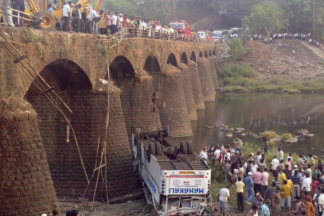 Rescuers and bystanders look at the wreckage of a passenger bus after it fell from a bridge in Ratnagiri district in the western Indian state of Maharashtra