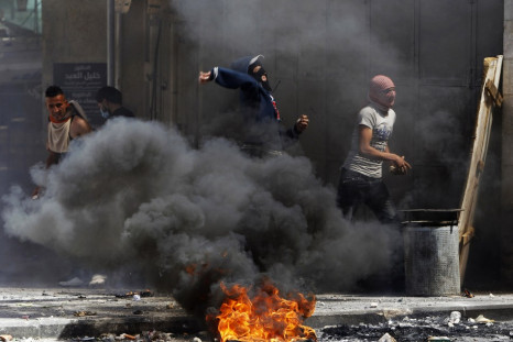 Palestinian protesters throw stones near a burning tyre during clashes with Israeli soldiers in the West Bank city of Hebron, after Maysara Abu Hamdeya