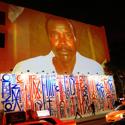 Passersby walk under a projection that is part of the non-profit organization Invisible Children's "Kony 2012" viral video campaign,