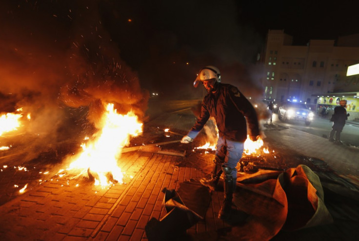 A riot police officer removes burning tyres from the highway set up by anti-government protesters in the village of Dira