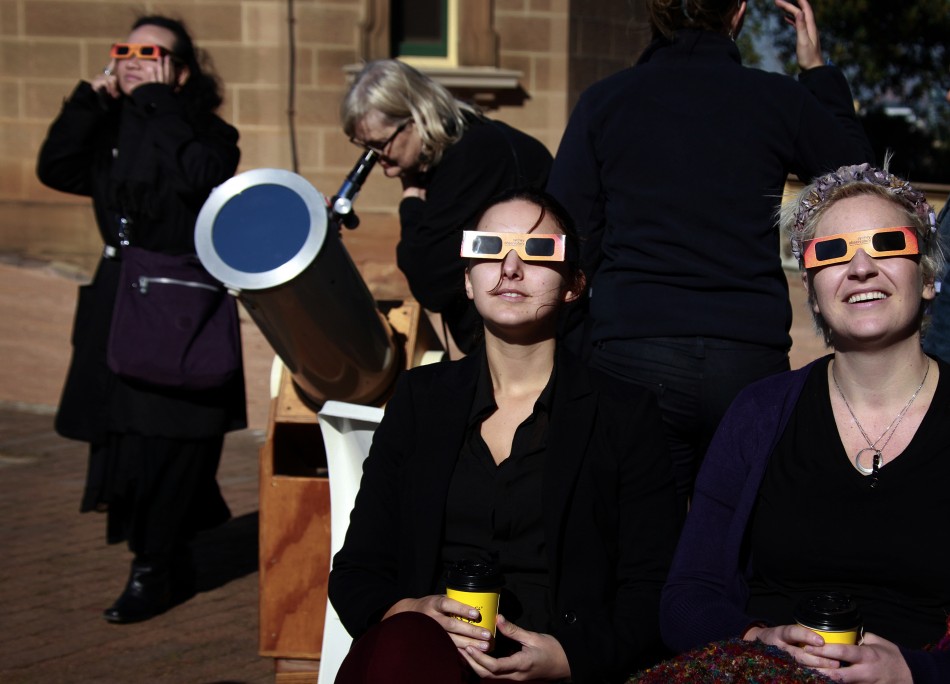 Women wearing protective glasses sit near another woman looking through a telescope at the annular solar eclipse from atop Observatory Hill in Sydney May 10, 2013.
